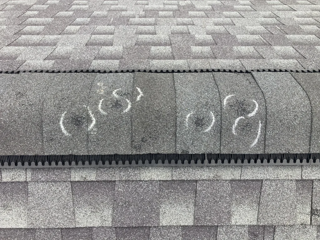 Chalk-circled hail impact marks on asphalt shingle ridge cap showing storm damage to a residential roof