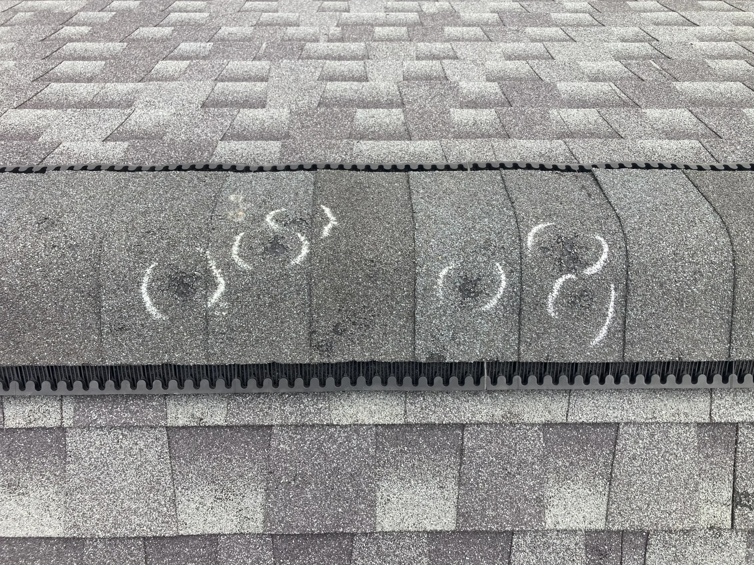 Chalk-circled hail impact marks on asphalt shingle ridge cap showing storm damage to a residential roof
