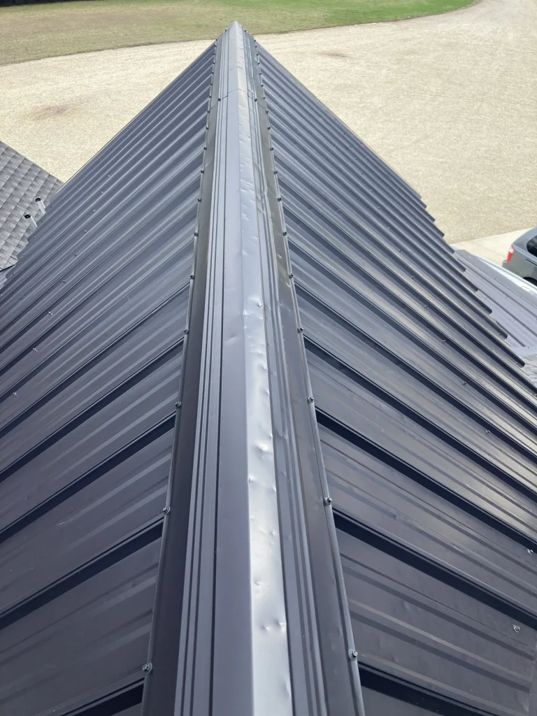 Hail damage dents visible along the ridge cap of a dark metal roof after a severe storm